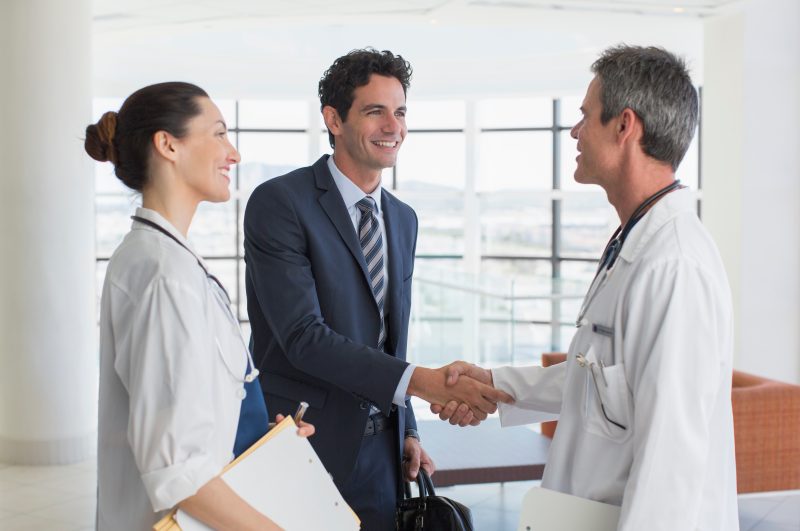 Doctor,And,Businessman,Handshaking,In,Hospital,Lobby