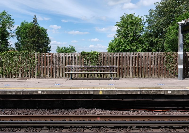 Train,Station,Platform,With,A,Wooden,Bench,And,Fence.,Trees