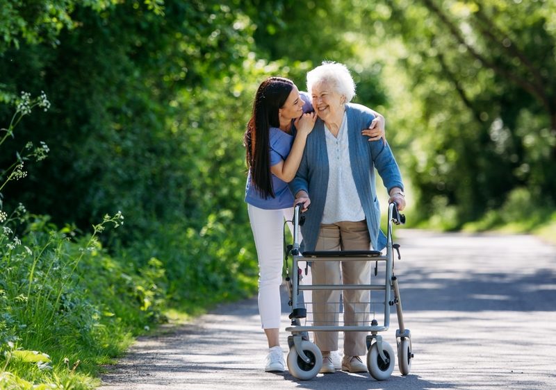 Female,Caregiver,And,Senior,Woman,With,Walker,On,Walk,In