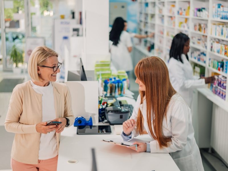 Senior,Woman,Chats,With,A,Pharmacist,At,A,Pharmacy,Counter,