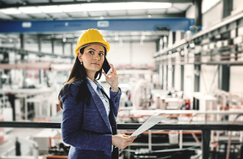 Female,Project,Manager,Standing,In,Modern,Industrial,Factory,Making,Phone