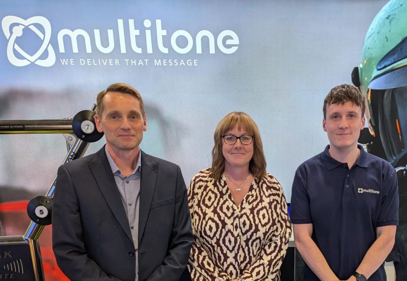 Multitone Marketing Team posing at a company exhibition stand with Multitone branding and a large emergency responder backdrop.