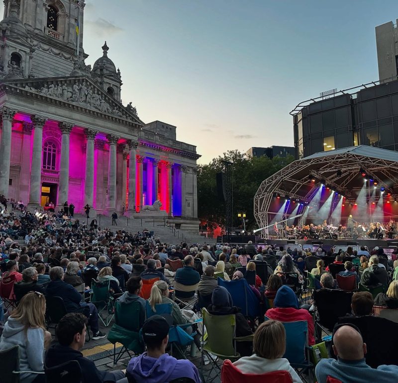 Concert audience watching a live performance outside Portsmouth Guildhall at dusk.